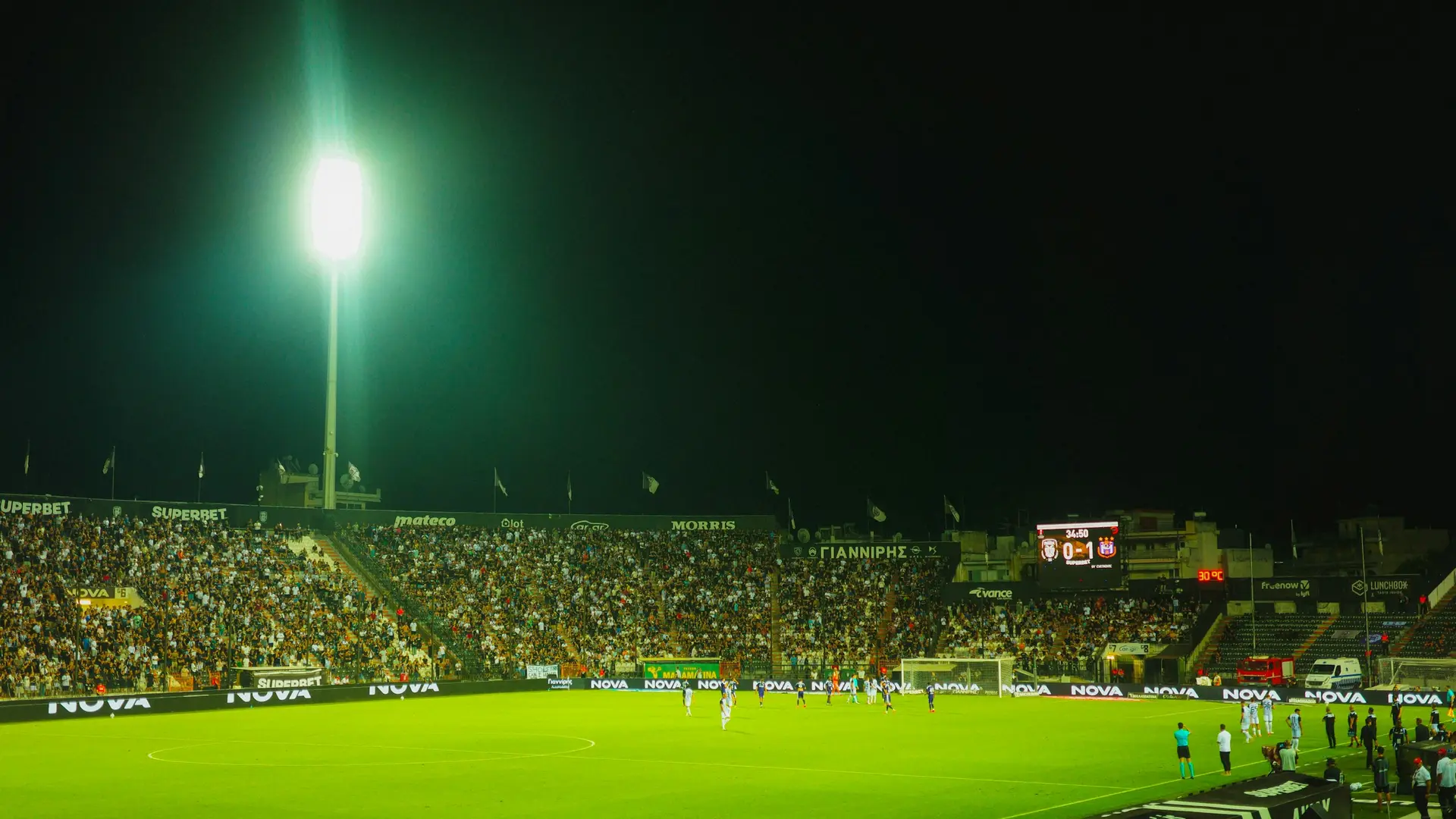 Ночной футбольный стадион под прожекторами, идёт матч